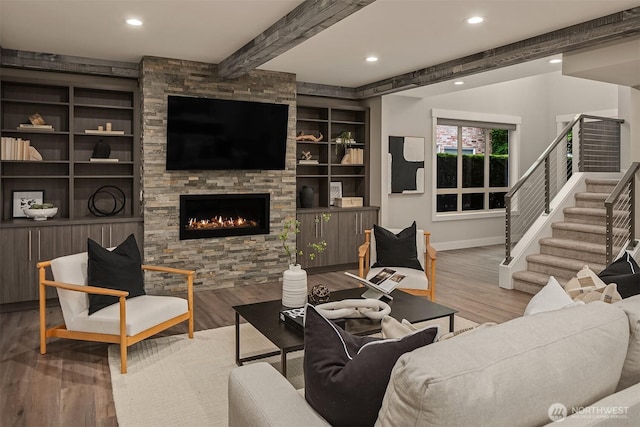 living room with stairs, wood finished floors, beam ceiling, a fireplace, and baseboards