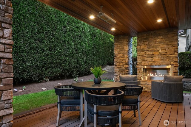 wooden deck with outdoor dining space and an outdoor stone fireplace