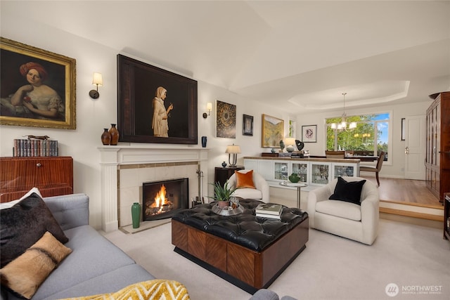 living room with carpet floors, a raised ceiling, a chandelier, and a fireplace