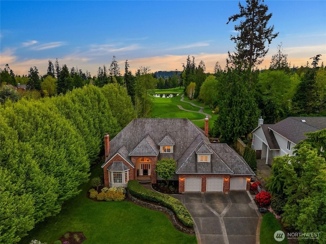 view of front of home with an attached garage, a lawn, driveway, and a chimney