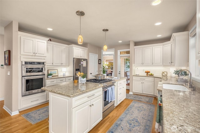 kitchen with high end appliances, a kitchen island, light wood-style floors, white cabinets, and a sink