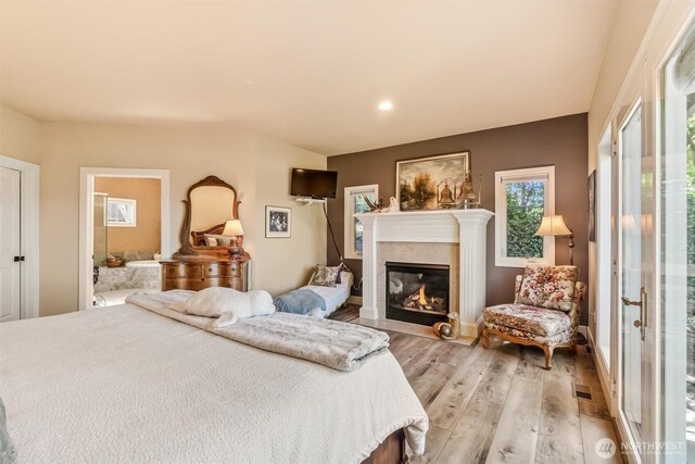 bedroom with a tiled fireplace, light wood-style flooring, and ensuite bathroom