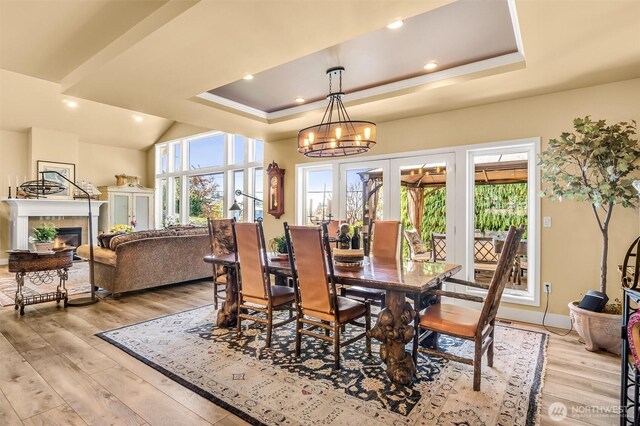 dining room featuring baseboards, light wood finished floors, a notable chandelier, a glass covered fireplace, and a tray ceiling