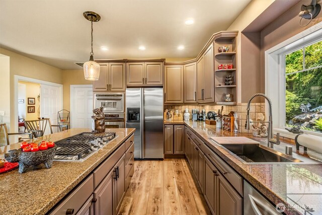 kitchen with open shelves, hanging light fixtures, a sink, stainless steel appliances, and light wood-type flooring