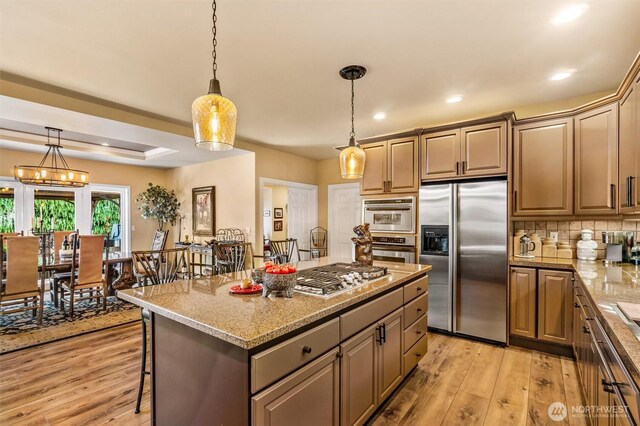 kitchen featuring backsplash, a center island, hanging light fixtures, light wood finished floors, and stainless steel appliances