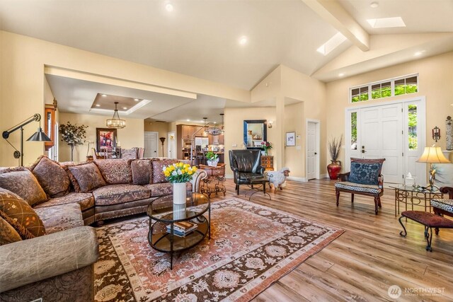 living area with beam ceiling, light wood finished floors, high vaulted ceiling, a chandelier, and a skylight