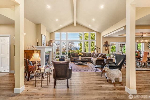 living room with a glass covered fireplace, wood finished floors, a healthy amount of sunlight, and beamed ceiling