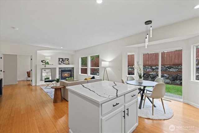 kitchen with a kitchen island, a fireplace, light wood-type flooring, white cabinets, and hanging light fixtures