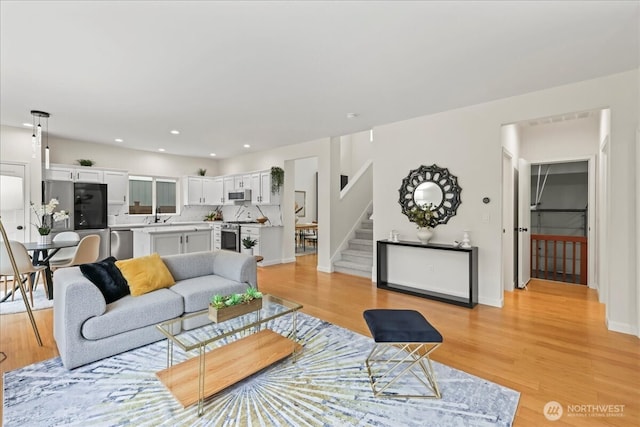 living room featuring light wood-style floors, recessed lighting, stairs, and baseboards