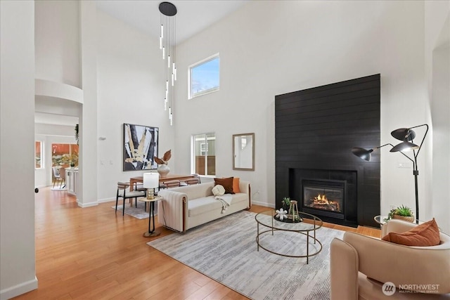 living area featuring a glass covered fireplace, baseboards, light wood finished floors, and a towering ceiling