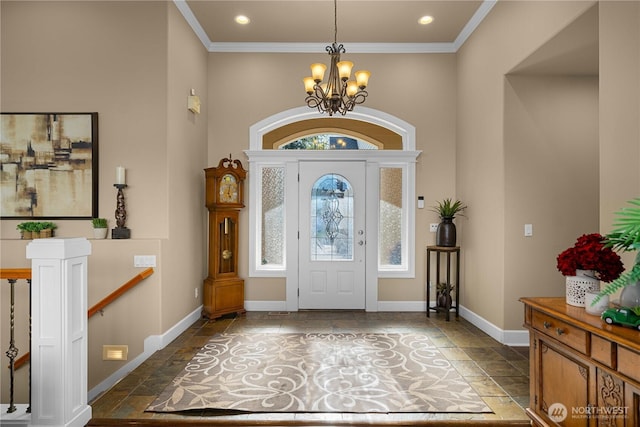 foyer entrance featuring an inviting chandelier, stone tile floors, crown molding, baseboards, and a towering ceiling