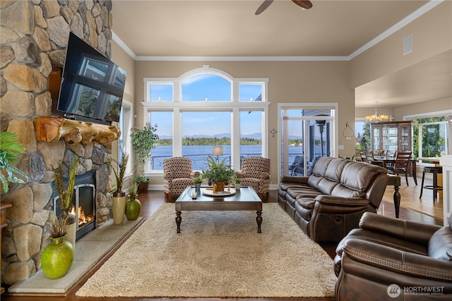 living area with wood finished floors, ceiling fan with notable chandelier, a stone fireplace, and crown molding