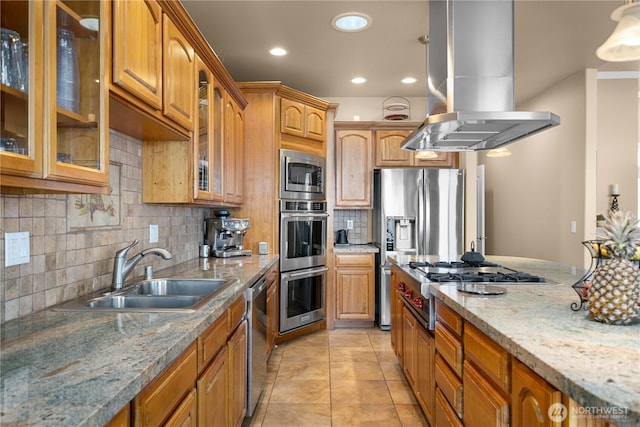kitchen featuring a sink, island range hood, appliances with stainless steel finishes, brown cabinetry, and backsplash