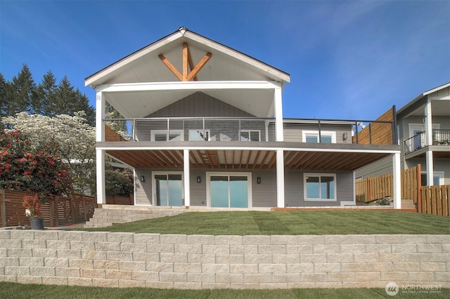 rear view of property featuring a lawn, fence, and a balcony