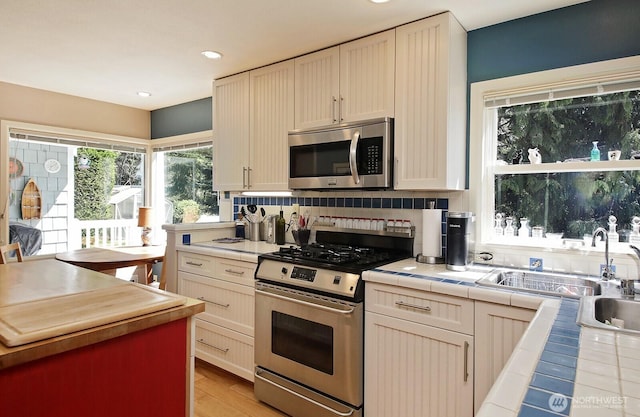 kitchen with decorative backsplash, tile countertops, appliances with stainless steel finishes, a sink, and recessed lighting