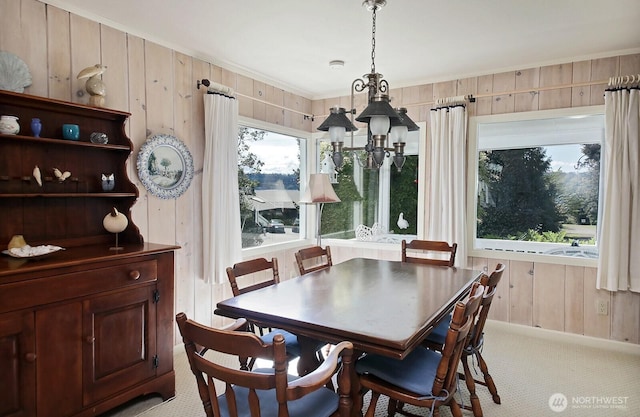 dining room with wooden walls, ornamental molding, and light carpet