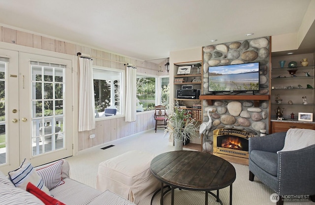 carpeted living room featuring wooden walls, visible vents, and a stone fireplace