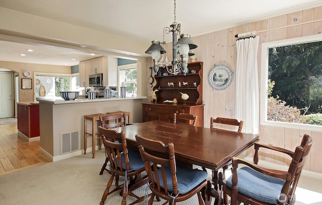 dining area with visible vents, arched walkways, wooden walls, and a notable chandelier
