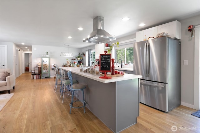 kitchen with island exhaust hood, light wood-type flooring, a breakfast bar area, white cabinetry, and freestanding refrigerator