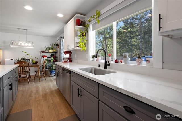 kitchen with light stone counters, stainless steel dishwasher, a sink, light wood-style floors, and gray cabinets