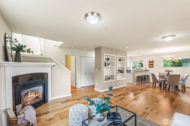 living room featuring baseboards, a notable chandelier, a fireplace, and light wood-style floors