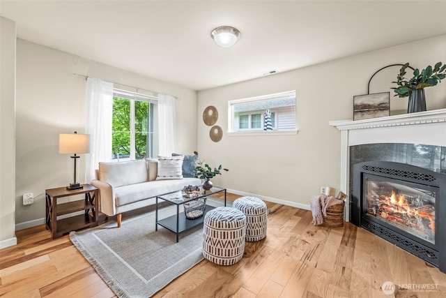 living area with light wood-type flooring, a tiled fireplace, and baseboards