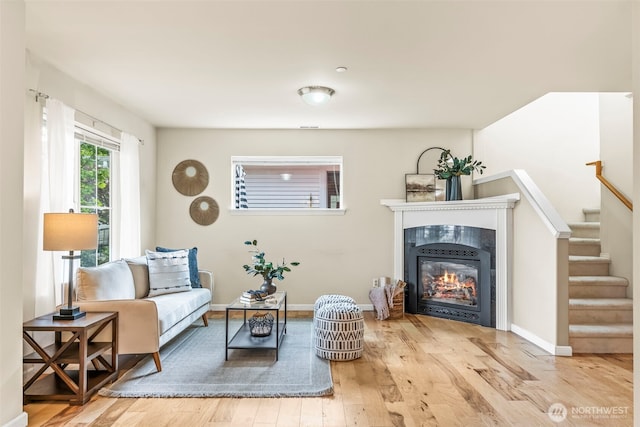 sitting room with a tiled fireplace, wood finished floors, baseboards, and stairway