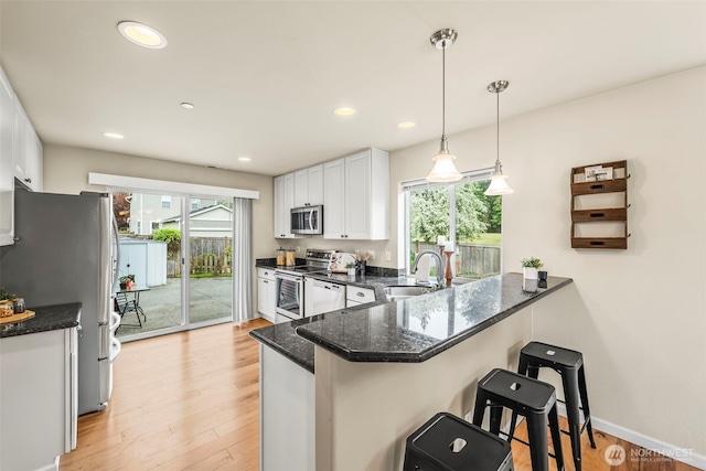 kitchen with a peninsula, a sink, stainless steel appliances, a kitchen breakfast bar, and white cabinetry