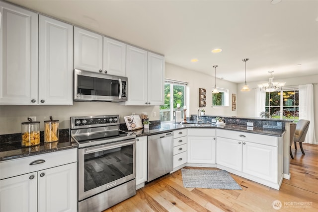 kitchen with a sink, a peninsula, stainless steel appliances, light wood-style flooring, and white cabinets