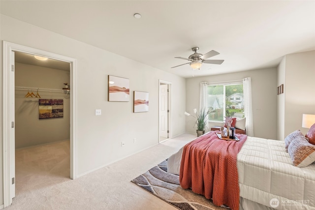 bedroom featuring light colored carpet, a walk in closet, baseboards, and a ceiling fan