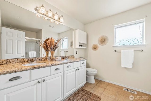 bathroom with double vanity, toilet, a sink, visible vents, and baseboards