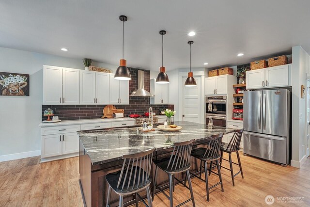 kitchen featuring appliances with stainless steel finishes, backsplash, white cabinets, and wall chimney range hood