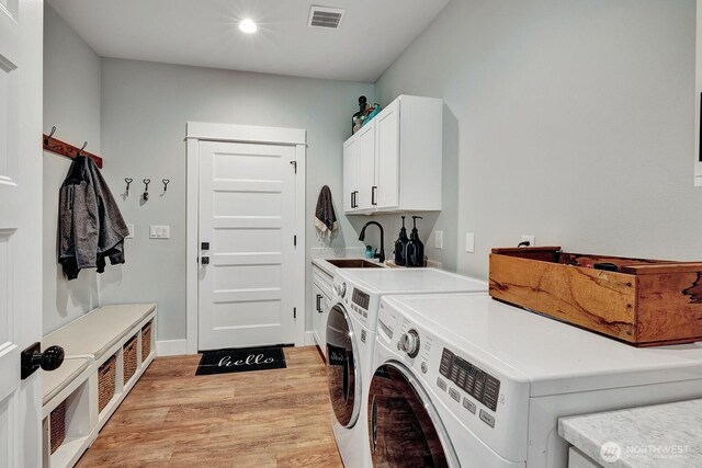 washroom featuring cabinet space, washer and dryer, a sink, light wood-style floors, and visible vents