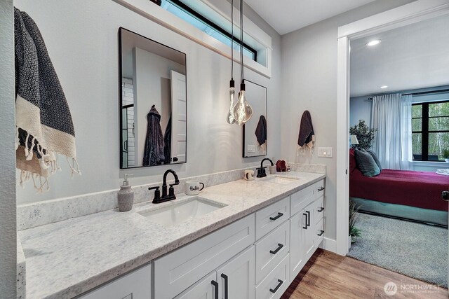 full bath featuring a sink, double vanity, wood finished floors, and connected bathroom