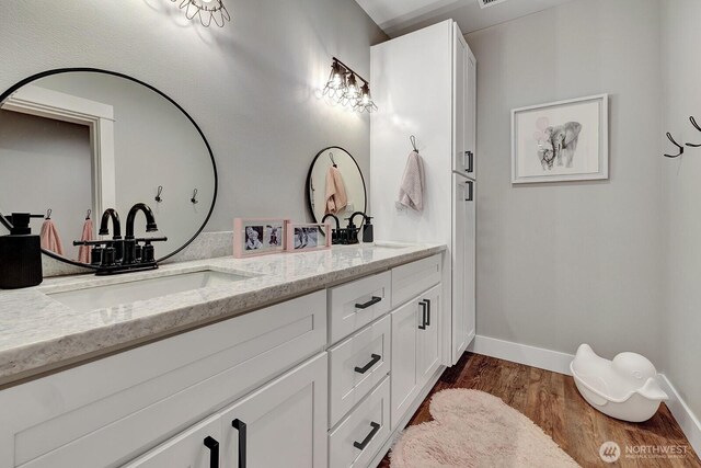 bathroom with a sink, baseboards, double vanity, and wood finished floors