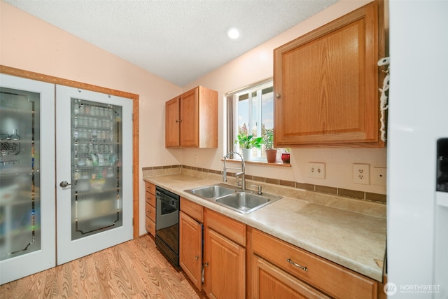 kitchen with black dishwasher, light countertops, a textured ceiling, a sink, and light wood-style flooring