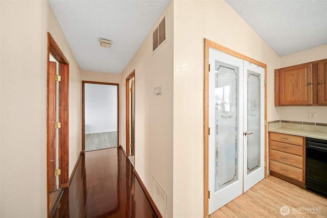 hallway featuring light wood-type flooring, a textured ceiling, and visible vents