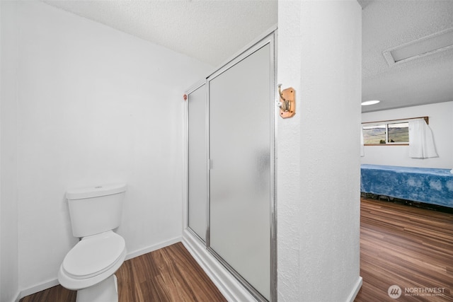 full bathroom with a textured ceiling, a stall shower, wood finished floors, toilet, and connected bathroom