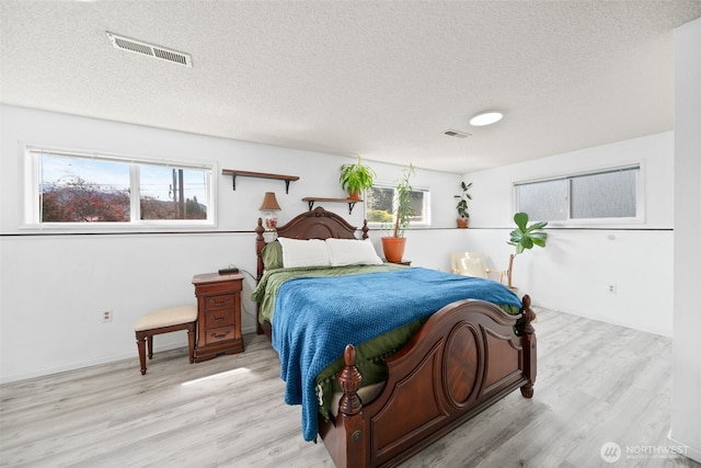 bedroom with a textured ceiling, visible vents, multiple windows, and light wood-style floors