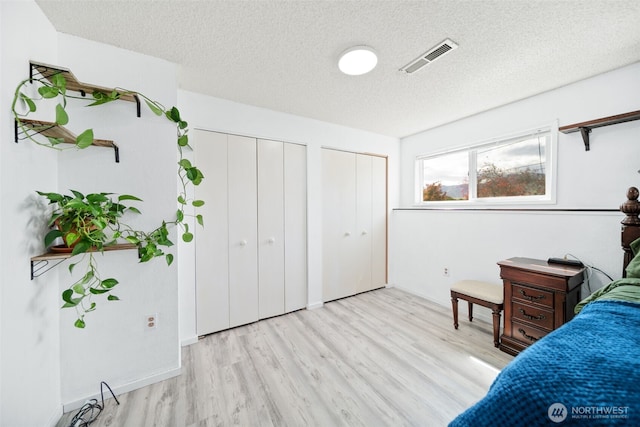 bedroom featuring two closets, light wood finished floors, a textured ceiling, and visible vents