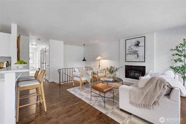 living room featuring dark wood-type flooring, baseboards, and a brick fireplace