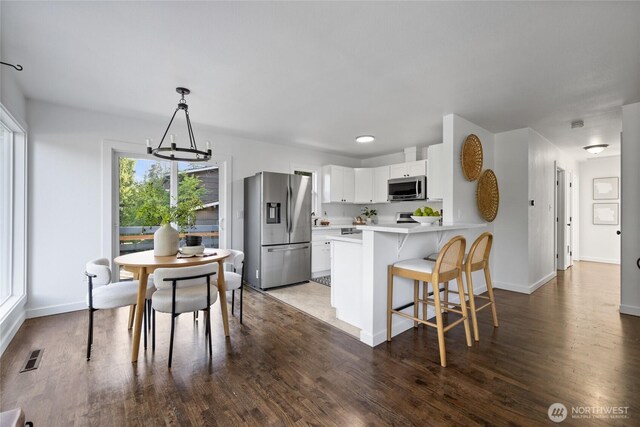 kitchen featuring an inviting chandelier, dark wood-style flooring, a peninsula, light countertops, and appliances with stainless steel finishes