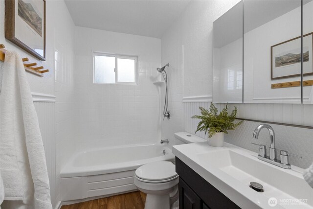 bathroom with bathtub / shower combination, wainscoting, wood finished floors, vanity, and toilet
