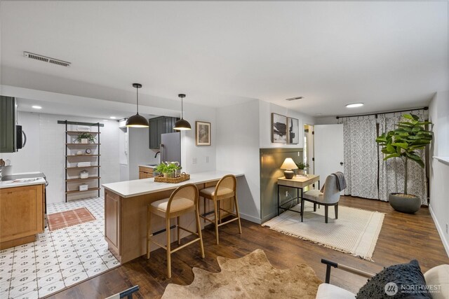 kitchen with light countertops, a peninsula, a kitchen bar, visible vents, and pendant lighting