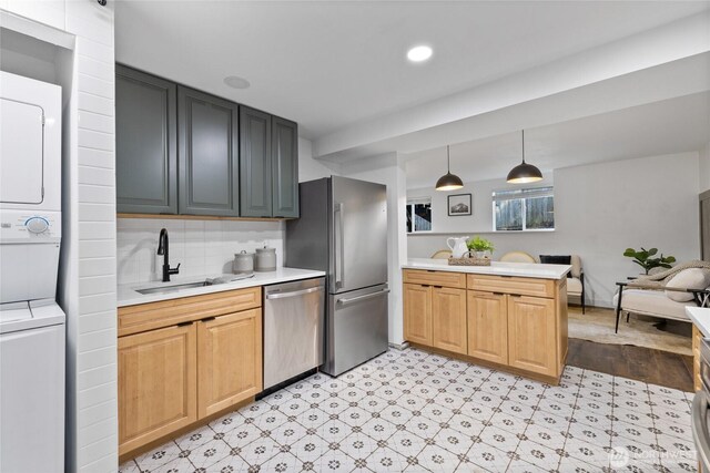 kitchen featuring a peninsula, stacked washer / dryer, light countertops, a sink, and appliances with stainless steel finishes