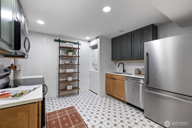 kitchen featuring a sink, light countertops, light floors, stacked washer and clothes dryer, and stainless steel appliances