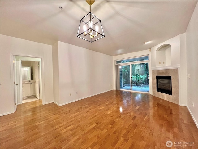 unfurnished living room with a notable chandelier, baseboards, wood finished floors, and a fireplace