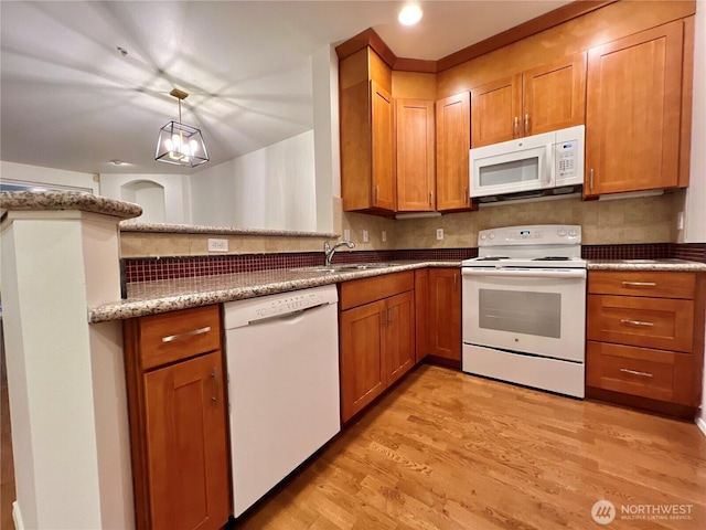 kitchen with white appliances, decorative backsplash, brown cabinetry, light wood finished floors, and a sink