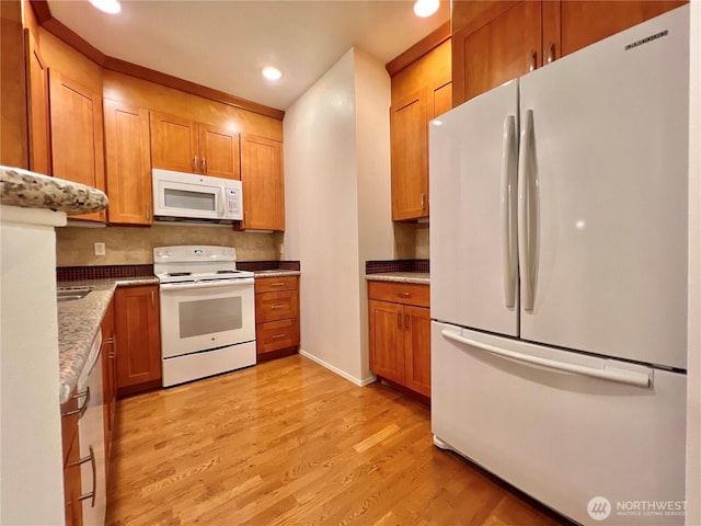 kitchen with recessed lighting, brown cabinets, light wood-style floors, and white appliances