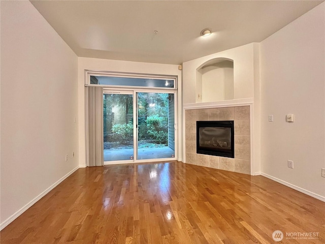unfurnished living room featuring a tile fireplace, wood finished floors, and baseboards